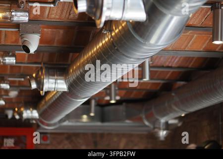 Impianti industriali a vista e tubi HVAC su soffitto in mattoni con telecamera di sicurezza in un interno moderno Foto Stock