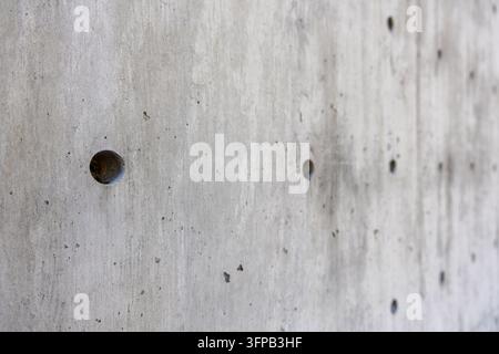 Una rientranza circolare si distingue in primo piano su un muro di cemento grigio mentre rientranze aggiuntive e segni superficiali si allontanano in una morbida sfocatura verso th Foto Stock