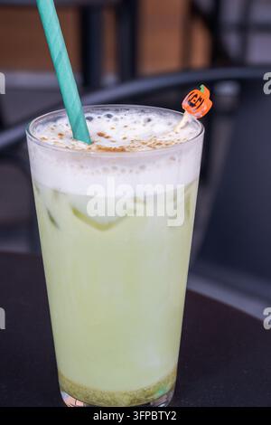 Un bicchiere rinfrescante di latte matcha ghiacciato a strati con schiuma bianca fredda, spolverato di cannella e servito con una cannuccia di carta verde accanto a un Ha giocoso Foto Stock