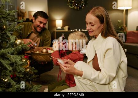 Famiglia felice con bambino che decora l'albero di Natale a casa Foto Stock