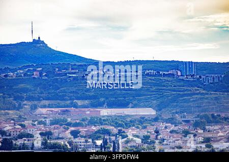 Grandi lettere bianche che compongono la parola Marseille si ergono su una collina sopra i quartieri residenziali e gli edifici industriali. Un traliccio di comunicazione si innalza da Foto Stock