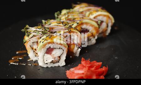 Rotoli di sushi con salmone, avocado, tonno, crema di formaggio, microverdi, semi di sesamo e salsa su un piatto di ardesia scuro Foto Stock