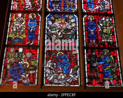 WORMS, GERMANIA - 27 MAGGIO 2025: Vivaci vetrate colorate della cattedrale di Worms che raffigurano più scene narrative bibliche con figure in rosso intenso Foto Stock