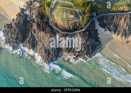 Vista aerea verso il basso di una scogliera rocciosa frastagliata con un sentiero pedonale sinuoso, riserva costiera, spiagge sabbiose e acqua oceanica limpida Foto Stock