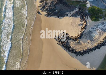 Vista aerea dall'alto di Owl Beach con ampia spiaggia sabbiosa, onde oceaniche delicate, frangiflutti roccioso curvo e riserva costiera ombreggiata Foto Stock