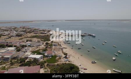 Vista aerea di Ilha do Farol con piccole barche ormeggiate nell'acqua limpida, spiaggia sabbiosa e case bianche a Faro, Faro, Portogallo. Foto Stock