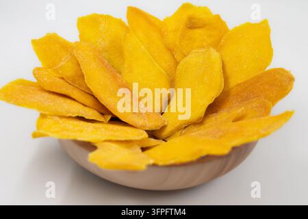 Fette di mango essiccate dorate in una ciotola di legno su superficie bianca Foto Stock