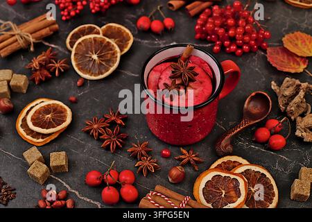 Vino caldo mulato in una tazza di ferro con spezie, zucchero bruciato, chiodi di garofano, noci, cannella, anice stellato, bacche di sorbo e bacche di rosa canina, natura morta astratta autunnale c Foto Stock