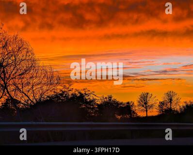Trascinante tramonto luminoso che tinge le nuvole di sfumature di arancione, rosa e nero Foto Stock
