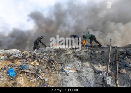 Tre uomini che lavorano tra le fiamme e il fumo nero e denso su un cumulo di rifiuti in fiamme, Regione di Greater Accra, Accra, Ghana Foto Stock