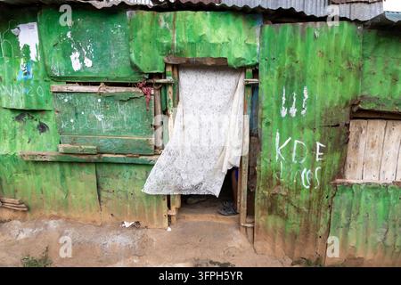 Muro in lamiera ondulata dipinto di verde patinato con una tenda di pizzo in una porta nell'area di Kibera, Contea di Nairobi, Nairobi, Kenya Foto Stock