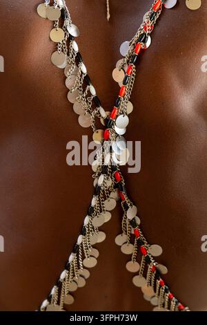 Primo piano dettagliato della schiena di un uomo della tribù Samburu decorato con catene incrociate di dischi in metallo argentato e perline rosse, nere e bianche su una pelle scura, S Foto Stock