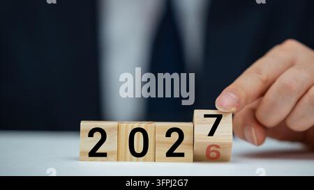 Mano che lancia un cubo per cambiare l'anno da 2026 a 2027 in un concetto aziendale. Foto Stock