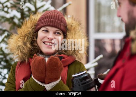 Donna caucasica di mezza età sorridente che beve tè caldo all'aperto con un uomo caucasico durante le vacanze invernali. Utile per il marketing delle bevande stagionali e vincita Foto Stock