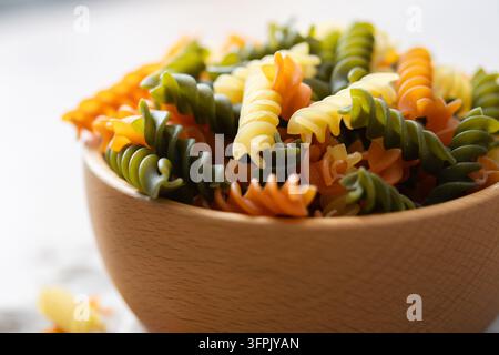 Pasta fusilli tricolore asciutta in una ciotola su tavolo di legno Foto Stock