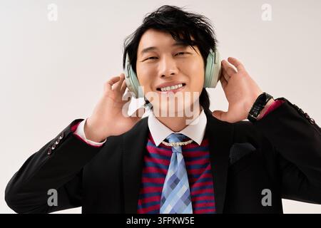 Giovane uomo indossa abiti alla moda, esprimendo gioia mentre ascolta musica al chiuso. Foto Stock