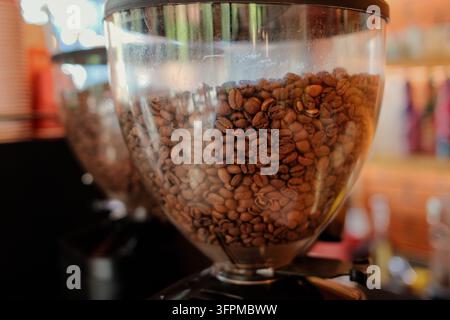 Prima di caffè tostati all'interno di un imbuto trasparente di un macinacaffè in un bar. I ricchi chicchi marroni e la bassa profondità di campo mettono in risalto il caffè Foto Stock