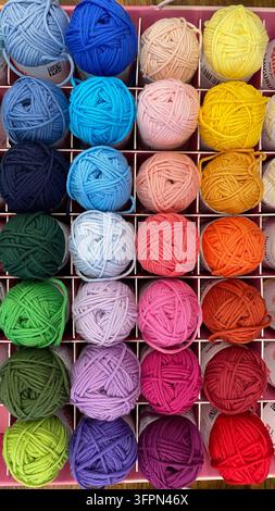 Palle di filo colorate disposte in una palette di colori arcobaleno in una scatola divisoria in un negozio di articoli per il fai-da-te, vista dall'alto Foto Stock