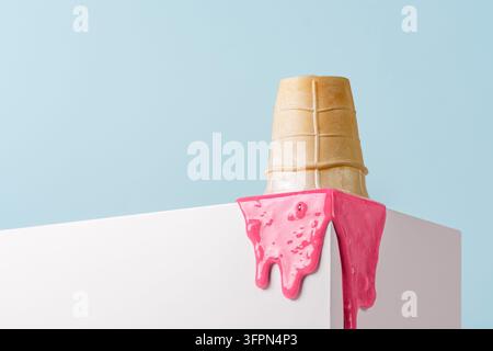 Tazza di waffle con gelato rosa che si scioglie sul bordo di un cubo bianco su uno sfondo blu pastello. Foto Stock