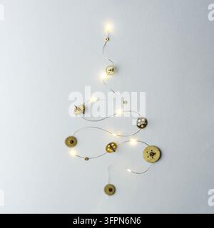 Una decorazione murale minimalista realizzata con ingranaggi metallici e luci a filo che formano un albero di Natale astratto su uno sfondo bianco. Creativo minimalista Ch Foto Stock