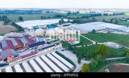 Vista aerea di un'azienda agricola e di un complesso di serre con digester biogassici, pannelli solari sui tetti e file di tunnel in plastica nelle terre rurali Foto Stock