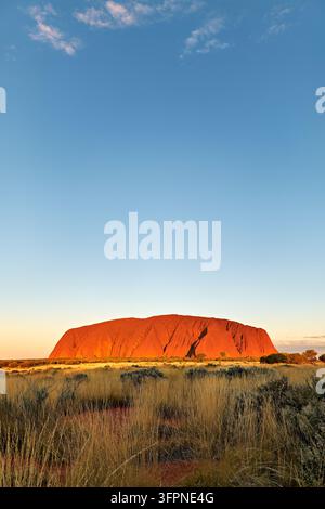 Monolito di arenaria rossa Uluru, o Ayers Rock, che brilla nella luce della sera sopra le praterie desertiche del Parco Nazionale di Uluru-Kata Tjuta, Australia centrale Foto Stock