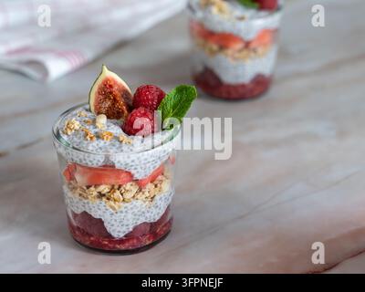 Parfait a strati individuale con fichi, lamponi, semi di chia e granola combinati con uno strato bianco cremoso e menta fresca per un dessert di frutta colorato. Foto Stock