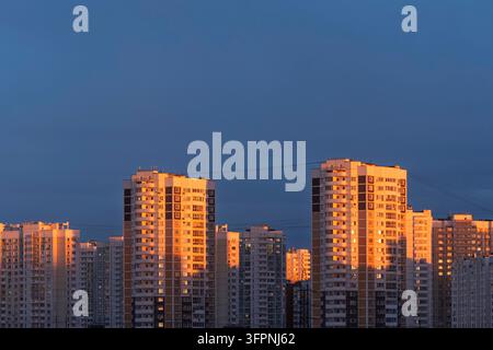 Gli edifici residenziali ad alto piano brillano nella calda luce del tramonto, creando una scena urbana serale calma con ombre profonde e contrasto ricco. Foto Stock