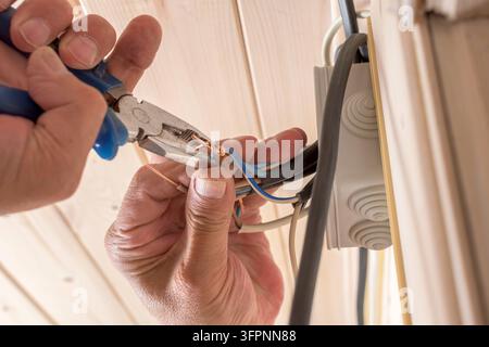 Primo piano di un elettricista che torce fili di rame con una pinza in una scatola di giunzione, mostrando precisione e riparazione elettrica domestica professionale. Foto Stock