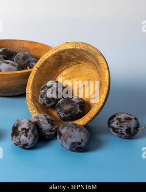 Prugne viola fresche disposte con una ciotola di legno su uno sfondo blu Foto Stock