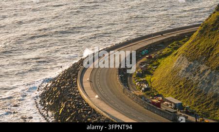 Vista aerea della strada costiera a Scarborough, con un muro di cinta curvo, un frangiflutti roccioso e scogliere erbose ripide lungo la costa a Scarborough Foto Stock
