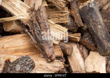 Primo piano di legna da ardere spaccata e tronchi grezzi impilati insieme, che mostrano la corteccia naturale, la venatura e le trame fibrose. Legna da ardere tradizionale preparata fo Foto Stock