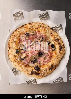 Mezza pizza con prosciutto, funghi, olive e cipolla rossa su foglio di carta, vista dall'alto con crosta tostata, formaggio fuso e parmigiano grattugiato visibili Foto Stock