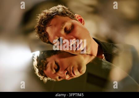 Uomo con gli occhi chiusi appoggiato a uno specchio per l'autoriflessione Foto Stock