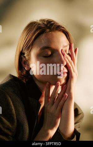 Donna che tocca il viso con gli occhi chiusi in studio per il benessere mentale Foto Stock