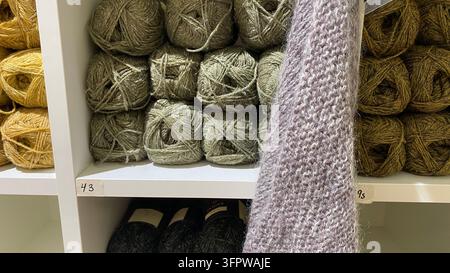 Campione di tessuto a maglia morbido appeso davanti a sfere di lana colorate su scaffali in un negozio di bricolage Foto Stock