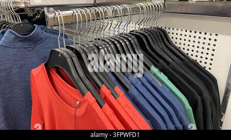 Camicie e top casual colorati disposti su appendiabiti neri in un negozio di abbigliamento usato Foto Stock
