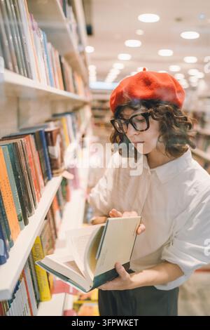 Giovane donna con un berretto rosso che sfoglia libri in una libreria Foto Stock