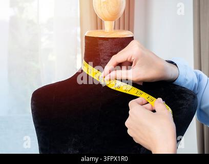 Primo piano delle mani di una giovane stilista asiatica che prende le misure su un manichino nel suo studio Foto Stock