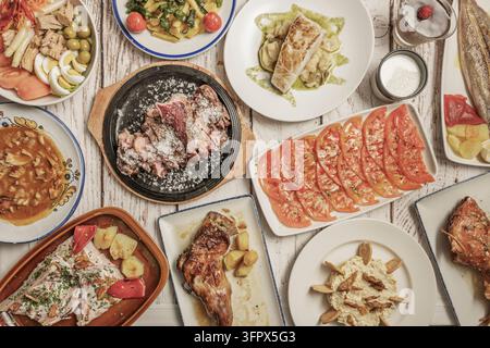 Tavolo sospeso di piatti tradizionali spagnoli: insalata di pomodori affettati, bistecca salata, merluzzo con patate, agnello arrosto, stufato, insalata di tonno e peperoni padron sopra Foto Stock