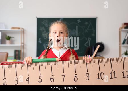Istruzione e progresso dell'apprendimento, studentessa sorpresa che tiene un enorme righello e una matita in una classe per lo sviluppo accademico e la crescita degli studenti Foto Stock