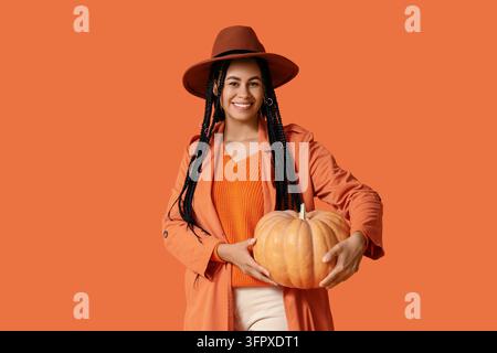 Raccolta autunnale e celebrazione stagionale, giovane donna sorridente che tiene una zucca per il Ringraziamento o la preparazione delle feste di Halloween su sfondo arancione Foto Stock