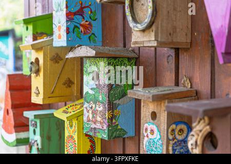 Cassette per uccelli in legno colorate sono appese a un muro di legno, decorate con personaggi del bosco, gufi e motivi floreali. Una cassetta nido centrale con una superficie consumata Foto Stock