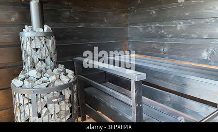 Stufa tradizionale per sauna a legna riempita con pietre e camino in metallo all'interno dell'interno in legno della sauna Foto Stock