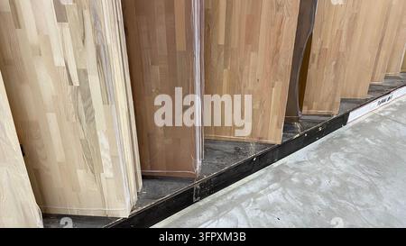 Grandi pannelli di legno chiaro avvolti in pellicola protettiva e esposti verticalmente su scaffali metallici nel negozio di legname Foto Stock