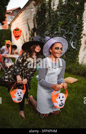 Due allegre ragazze che indossano costumi di Halloween che tengono i secchi in giardino Foto Stock