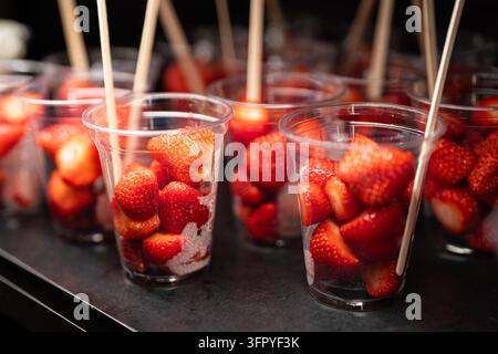 Fragole rosse mature confezionate in coppette trasparenti con stuzzicadenti di legno all'interno del frigorifero del caffè Foto Stock