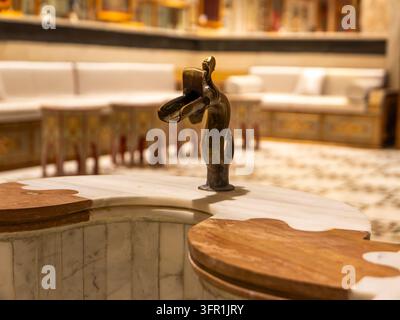 Prima vista di un beccuccio decorativo in bronzo a forma di creatura mitica montato su una vasca di fontana in marmo bianco. Foto Stock