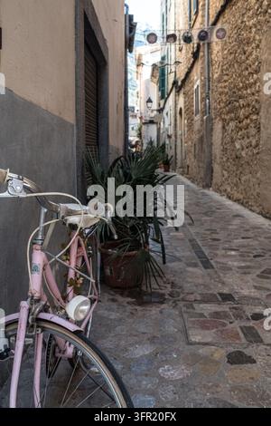 Una graziosa bicicletta rosa con una luce anteriore e decorazioni floreali è parcheggiata sul lato sinistro di un'angusta stradina di ciottoli a Valldemossa, Maiorca. La Foto Stock