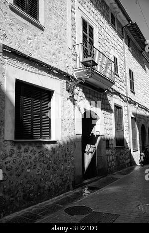 Foto in bianco e nero di edifici tradizionali in pietra che costeggiano una strada stretta a Valldemossa, Maiorca. La luce intensa crea ombre forti e hi Foto Stock